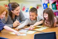 Teacher helping a group of kindergarten students with a project.