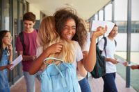 Two high school girls hug in the school hallway, celebrating their report cards