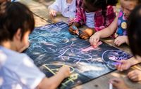 Preschool students drawing together with chalk on a large slate board