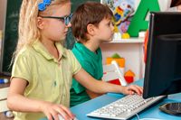 Two elementary students playing videogames on PCs