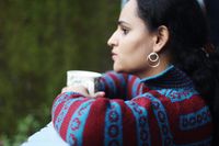 Woman looks thoughtfully out of a window with a cup of coffee in her hand