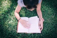 A middle school girl reading a book in a park on the grass