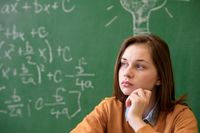 A teenage girl sitting in front of a blackboard with math formulas written on it, looking thoughtful