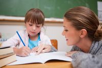 Teacher observing a young student as she writes in a notebook in class