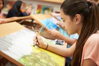 Student making a watercolor painting on a drawing table in art class