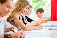 Students working on vocabulary lists at a long table in class