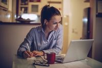 A teacher working on a laptop and notepad in her kitchen, preparing for the upcoming school year