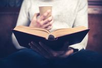 A man reading a book with a cup of coffee in his hand