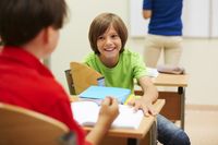 Two young boys smiling and talking with each other in a classroom