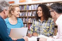 Four teachers talking at a professional development meeting in a library, working with papers and a laptop