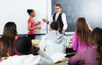 A math teacher working with a student in front of a diverse class