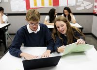 Students working in pairs together with laptops and handouts in class