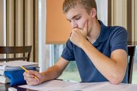 A teenage student studying at home at the dining table