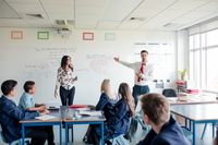 A university staff member presenting alongside a teacher in a high school class