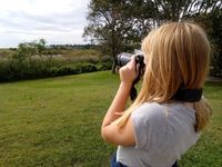 A student using a DSLR camera to photograph a landscape of a field and trees