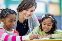 A teacher helping two elementary students with schoolwork