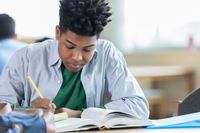 A high school student writing at a table in a Montessori-style class