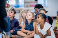 A group of diverse kindergarten students listening to their teacher read a story