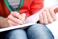 A close-up shot of a teenager writing in a notebook