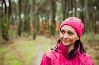 A woman walking through the woods in a pink rain jacket and knit hat