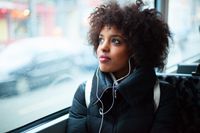 A woman rides a city bus, listening to a podcast on her headphones