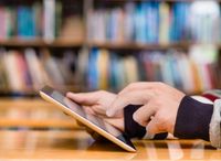 A close-up on a student's hands holding a tablet computer in a library