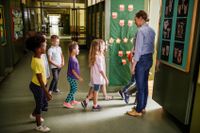 Happy female teacher welcoming elementary students in the classroom