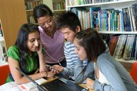 Group of senior teenage students together using portable audio player with a laptop computer in school reference library