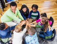 Elementary school students and their teacher sitting in a circle with their hands together in the middle