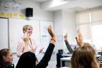 Teacher standing in front of students with their hands raised
