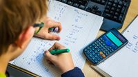 Teenage boy doing math homework with calculator and computer