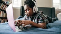 Boy using his laptop in his room with headphones on