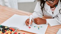 Girl in lab coat drawing an atom from a science experiment