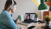 Woman drinking coffee during a video meeting at her desk at home