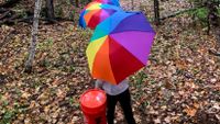 Elementary aged girl walks to her outdoor classroom carrying an umbrella and 5-gallon bucket