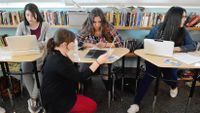 Teacher kneels down to help a student in 9th grade English class