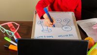 Student writing on a small whiteboard during a distance learning assignment
