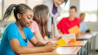 High school student reading a book while sitting at her desk in a classroom