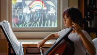Pre-teen boy practicing cello at home with rainbow painted on window