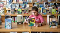 Elementary aged girl reading book in school library