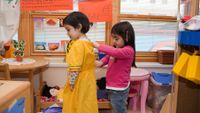 One girl helps another girl in pre-school class. 