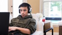 Teenage boy with headphones on couch on laptop