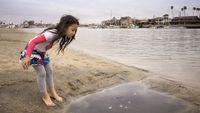 Girl looking into puddle on beach 