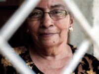 A closeup of an old woman's face with glasses framed by an outline of a white diamond shape.