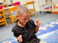 A young boy in a black shirt has his elbows against his sides and his hands raised in fists of excitement.