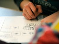 A closeup of a student's hand drawing flowers on a piece of paper with pen.