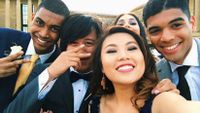 A group of five ethnic teens in formal wear are taking a selfie outside.