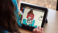 A girl is sitting at a desk looking at a tablet. We only see the back of her head. On the tablet screen is a color palette and a drawing of a brown and red farm.
