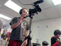 Boy wearing headphones standing in class operating a camera on a tripod