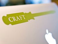 A closeup of the back of a Mac laptop showing the apple icon and a green sticker of a screwdriver that says, "Craft" in white lettering.